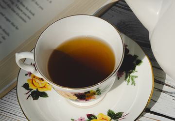 rose-decorated teacup and saucer beside an open book