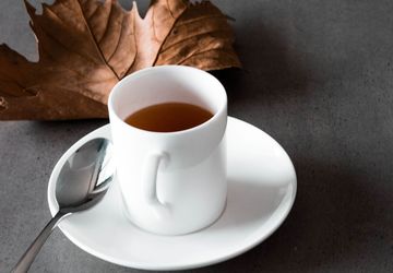 white teacup and saucer beside a brown autumn leaf