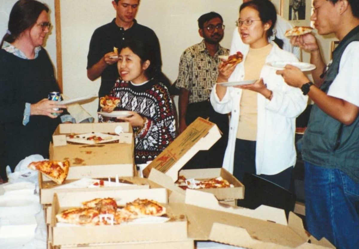 people gather around a table with stacks of pizzas